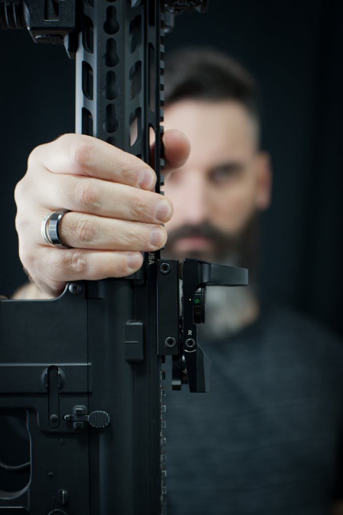 Soft focus of front part of big black gun in hand of anonymous pensive male with beard on blurred background